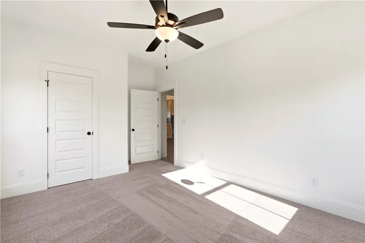 A well-lit bedroom with fresh carpeting and a classic ceiling fan, offering a clean canvas for personalization.