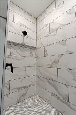 A pristine shower area featuring large format wall tiles and small hexagonal floor tiles.