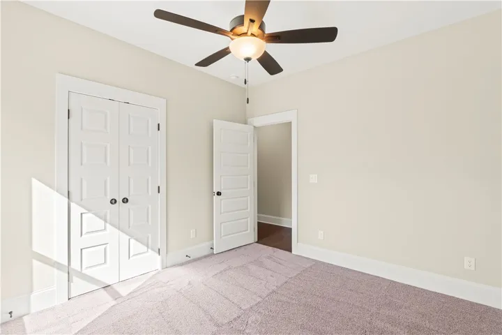 A comfortable bedroom with plush carpeting, offering ample space and a stylish ceiling fan.