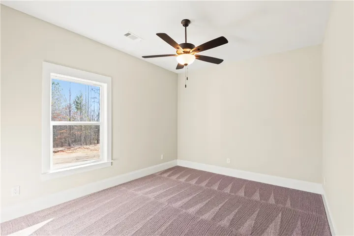 A well-lit bedroom features plush carpet and a window offering views of the surrounding natural landscape.