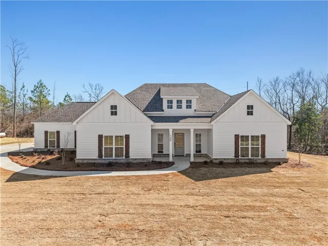 A striking white residence boasts classic dormer windows and a welcoming front porch, set against a backdrop of natural woodland.