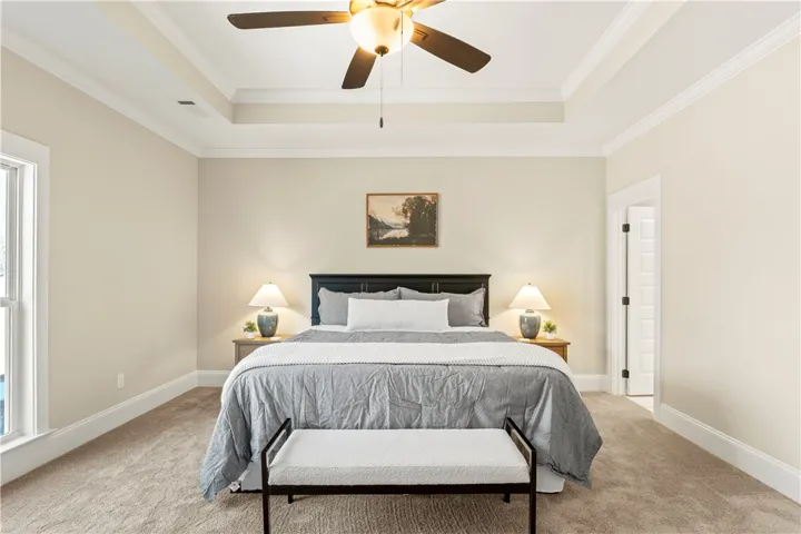 Experience tranquility in a well-lit bedroom featuring a tray ceiling, crown molding, and soft carpet underfoot.