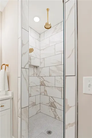 A striking walk-in shower features dual golden showerheads and elegant marble-patterned tile walls.