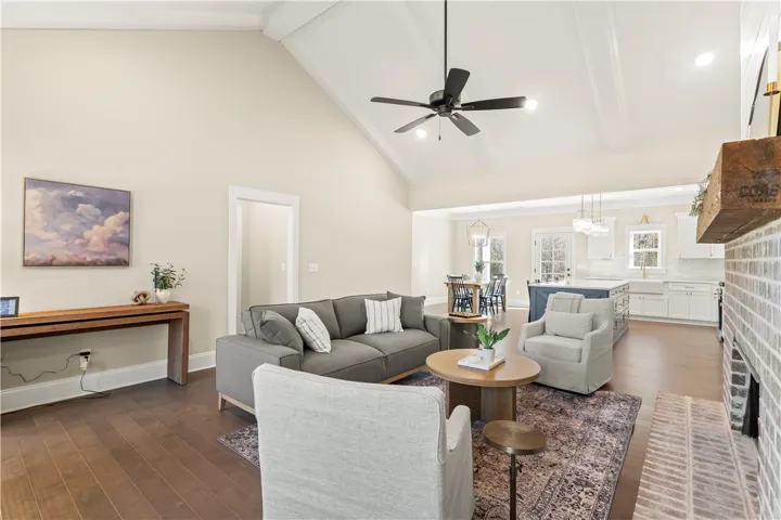 Hardwood floors stretch across this open-concept living space, anchored by a brick fireplace and soaring vaulted ceilings.