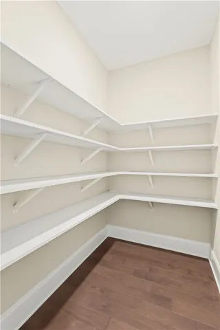 A corner pantry with ample shelving for organized storage, featuring warm hardwood flooring.