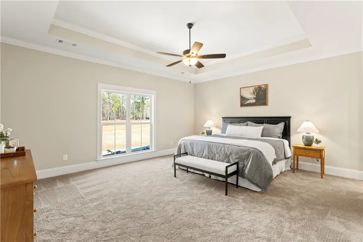 A spacious primary bedroom featuring a tray ceiling and a large window overlooking natural scenery.