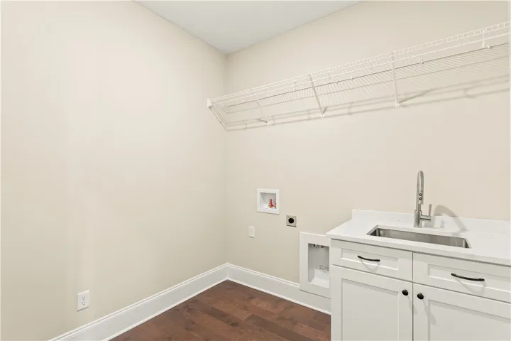 A well-appointed laundry space features dark hardwood flooring and a pristine sink with white cabinetry.