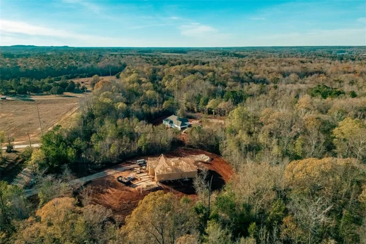 An aerial panorama reveals a vast, wooded estate with a new home under construction amidst mature trees.