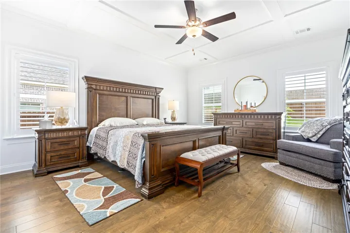 Elegant tray ceilings and beautiful hardwood floors complement this spacious, light-filled primary bedroom.