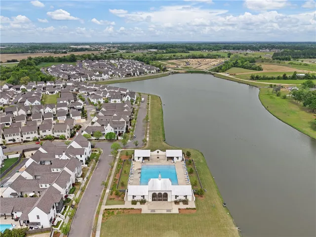 An aerial panorama reveals a picturesque residential community nestled alongside a serene lake, featuring a communal swimming pool.