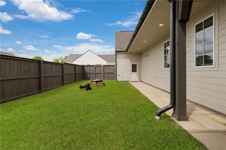 A well-maintained lawn offers ample space for outdoor enjoyment, bordered by a privacy fence and a practical patio.
