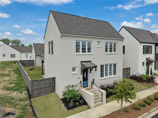 A charming white brick facade welcomes guests with a vibrant blue front door and a neat front yard.