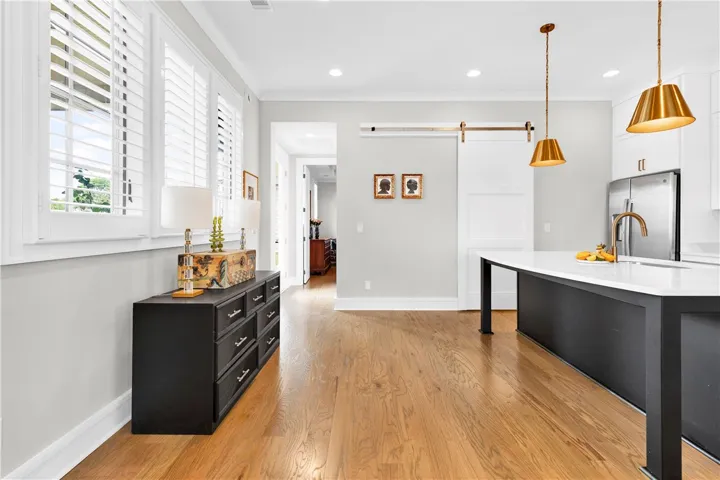 Golden hardwood floors extend through this open-concept space, leading to a modern kitchen island and elegant fixtures.