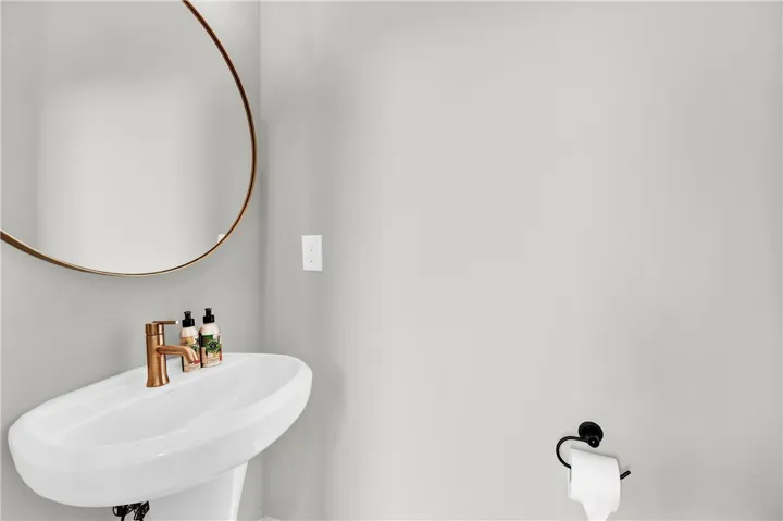 A sleek pedestal sink and contemporary round mirror offer refined simplicity in this compact bath.