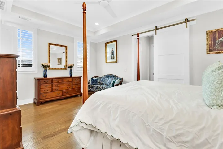 Hardwood floors and a tray ceiling define this restful bedroom, featuring a sliding barn door for streamlined access.