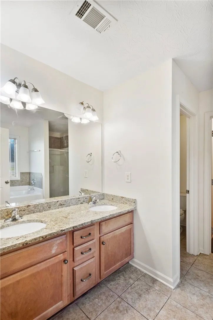 This bathroom offers a double vanity with granite counters and a separate area with a soaking tub.
