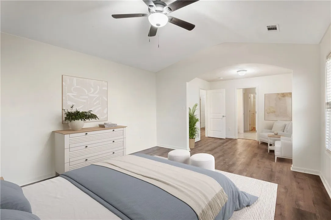 A generous primary bedroom features rich LVP flooring, an arched entry to a sitting area, and a ceiling fan for comfort.