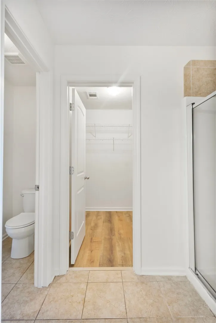 This functional bathroom features practical flooring, a toilet, and an accessible walk-in closet for everyday convenience.