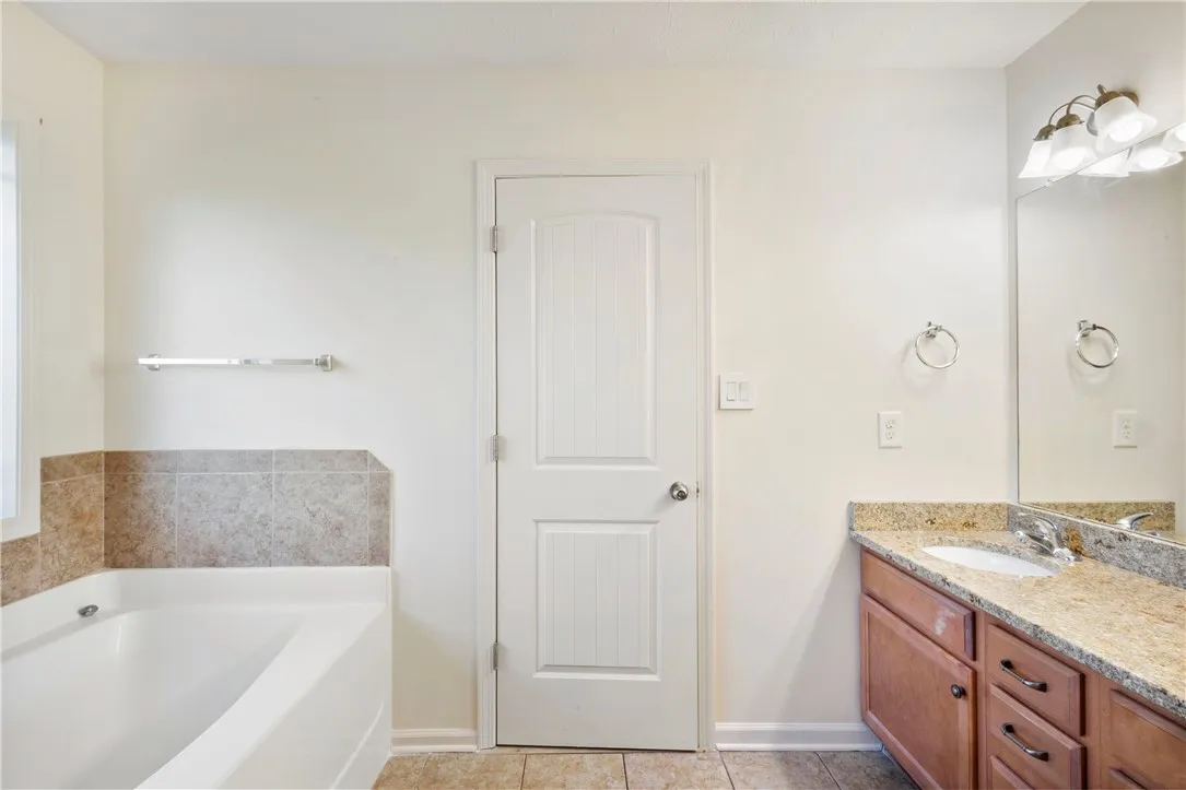 This bathroom features a soaking tub and a vanity with granite countertops, offering comfort and style.