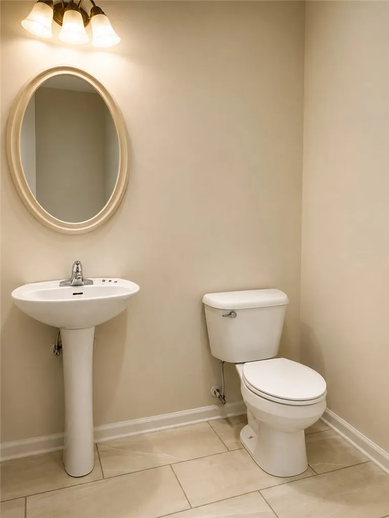 A well-appointed powder room features a classic pedestal sink and toilet, complemented by clean tile flooring.