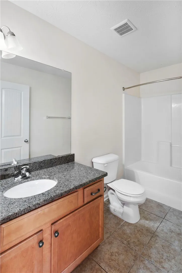 This bright bathroom features a vanity with a granite countertop and a shower-tub combination.