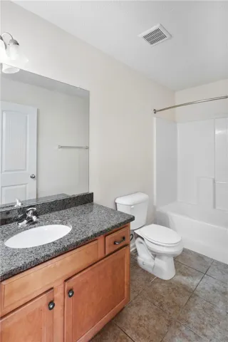 This bright bathroom features a vanity with a granite countertop and a shower-tub combination.