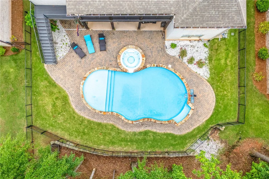 An aerial perspective reveals a private pool with an integrated spa, surrounded by a brick paver patio and lush green lawn.