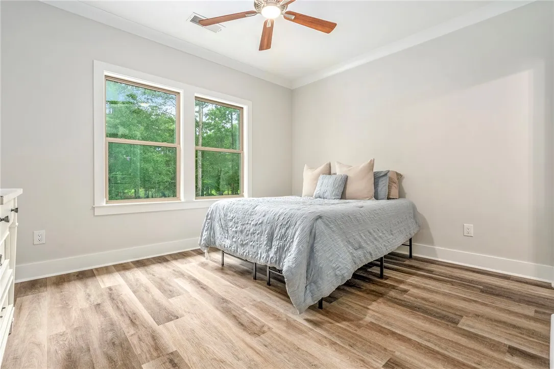A tranquil bedroom with wood-look flooring and ample natural light from large windows.