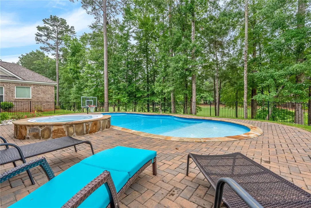 An inviting backyard oasis features a freeform pool, integrated spa, and expansive paver patio, all framed by mature trees.