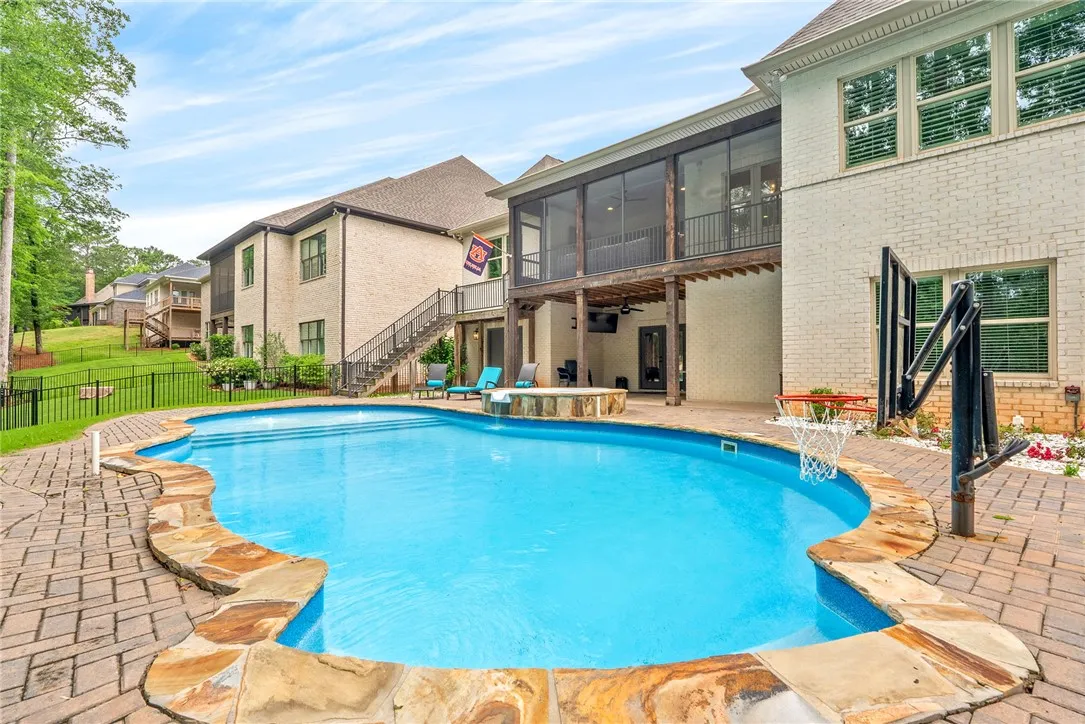 An inviting backyard oasis offers a freeform swimming pool with a hot tub and an elevated screened porch for relaxation.