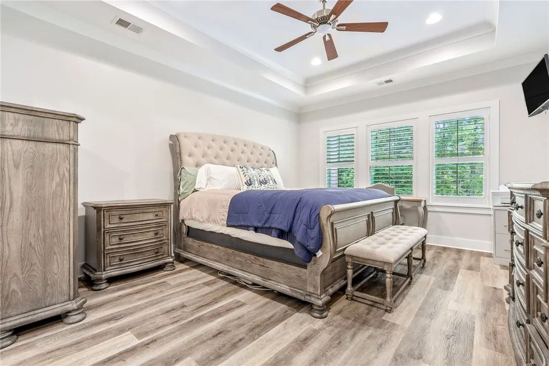 Elegant tray ceilings and wood-look flooring distinguish this spacious primary bedroom.
