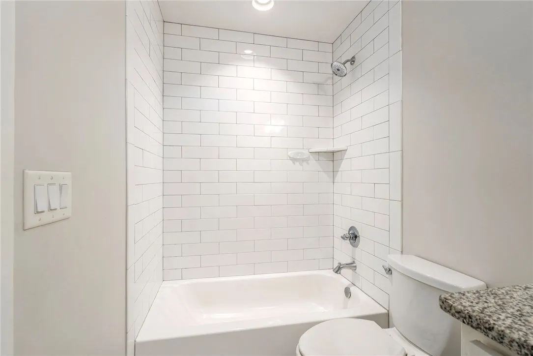 White subway tile adorns the bath and shower area, featuring a recessed light for focused illumination.