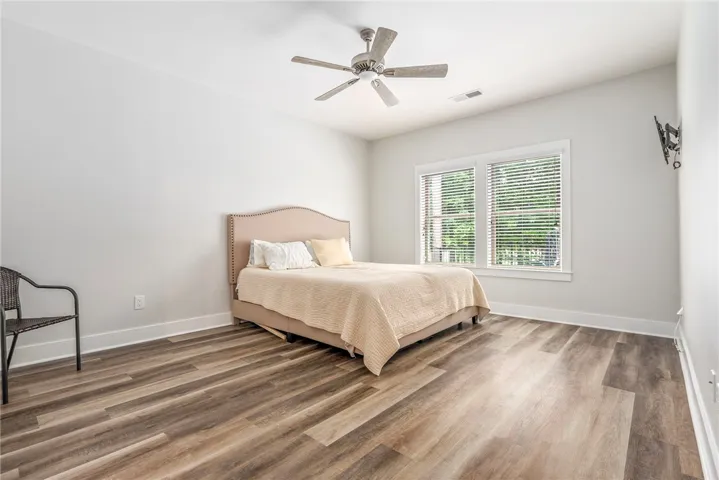 Well-lit sleeping quarters with a ceiling fan, featuring durable wood-look flooring and two bright windows.