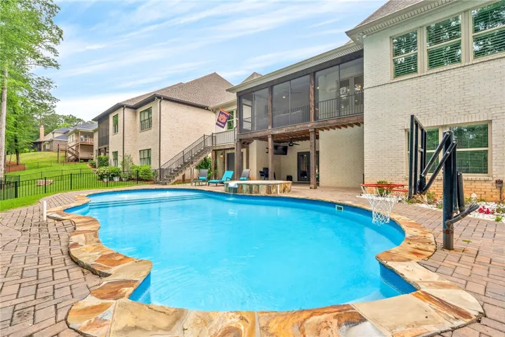 An inviting backyard oasis offers a freeform swimming pool with a hot tub and an elevated screened porch for relaxation.