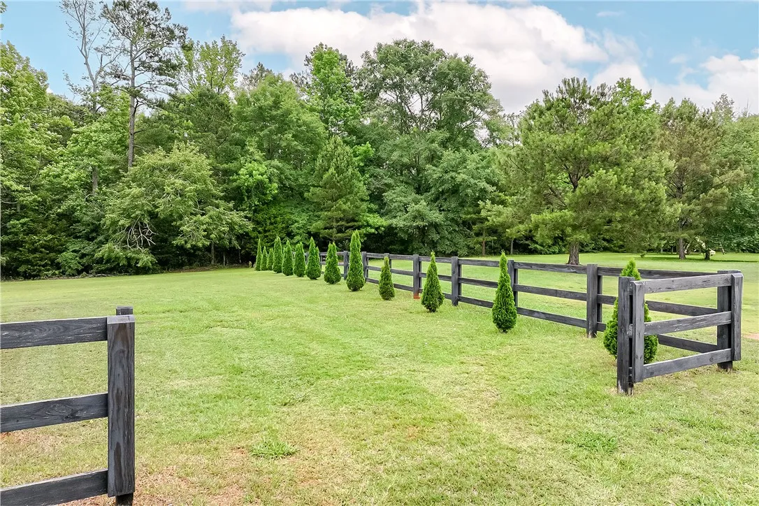 A dark-stained wooden fence defines the property line, backed by a lush tree line and punctuated by a row of small evergreens.