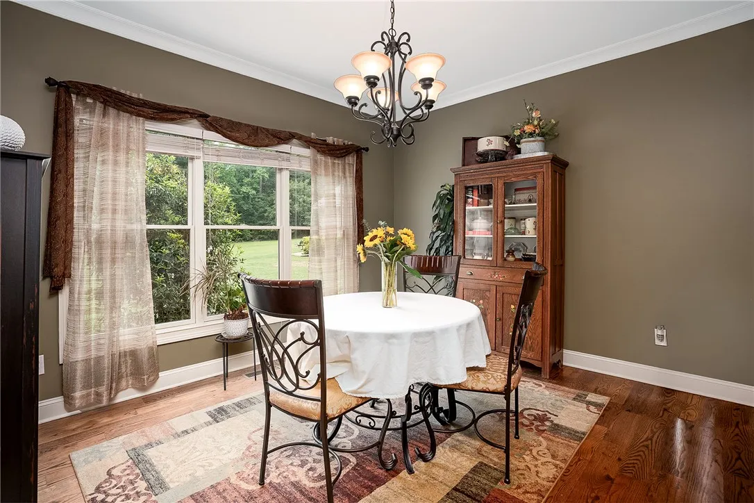 Elegant dining space, illuminated by an ornate chandelier, showcases rich hardwood floors and a view of lush greenery.