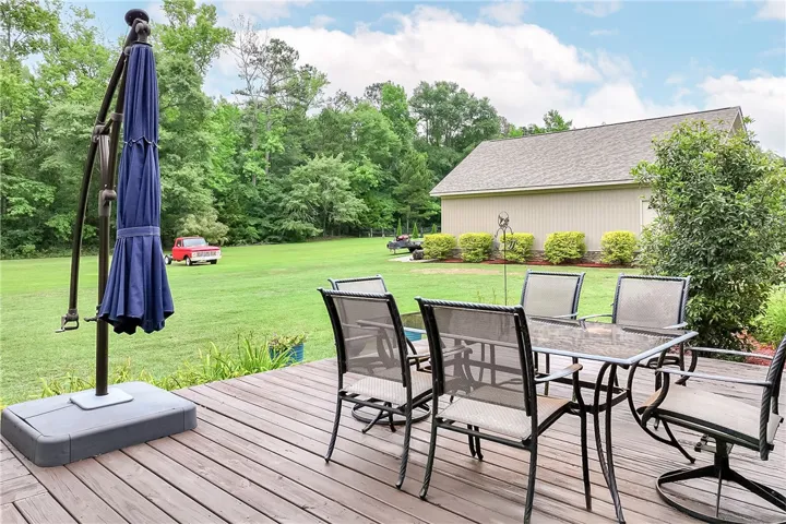 A spacious wooden deck with an outdoor dining set provides a private backyard retreat with lush, mature trees.