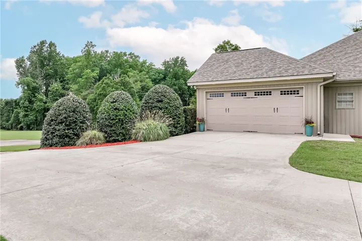 A well-maintained concrete driveway leads to a two-car garage, framed by manicured landscaping and lush greenery.