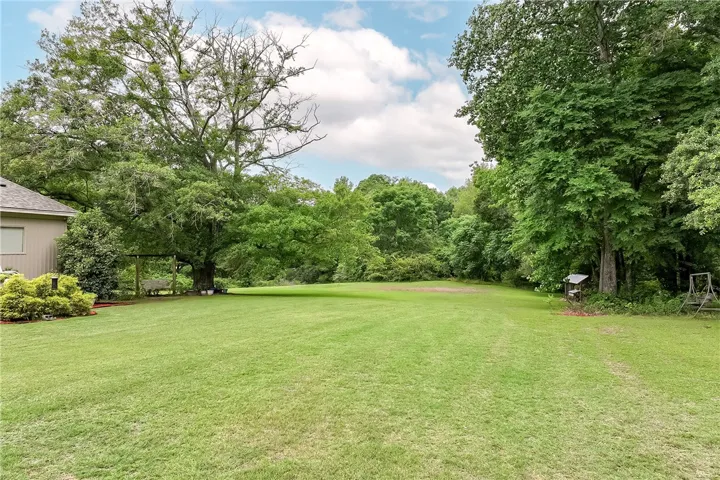 An expansive green yard framed by towering trees offers a serene natural setting.