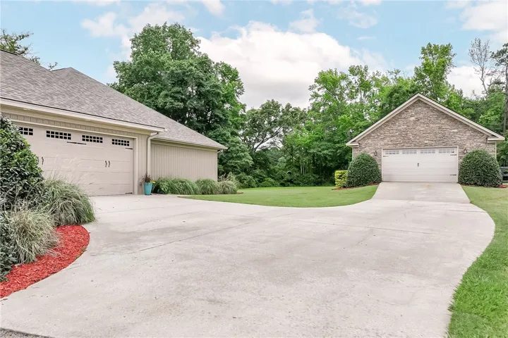 A winding concrete driveway leads to two separate garages, set against a backdrop of mature trees and a manicured lawn.