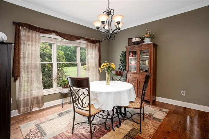 Elegant dining space, illuminated by an ornate chandelier, showcases rich hardwood floors and a view of lush greenery.