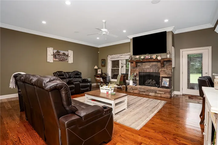 A welcoming living area showcases rich hardwood flooring, a substantial stone fireplace, and pristine crown molding.