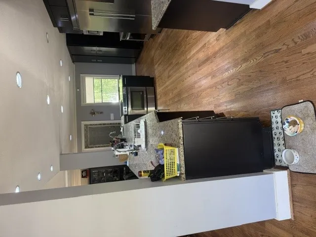 A contemporary kitchen features rich hardwood flooring, a central island with granite counters, and recessed lighting.