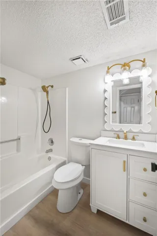 A well-lit bathroom features a white vanity, a clean bathtub, and a modern toilet.