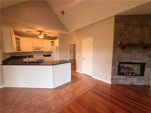 A well-appointed kitchen with black countertops and white cabinetry overlooks a living area with a stone-clad fireplace.