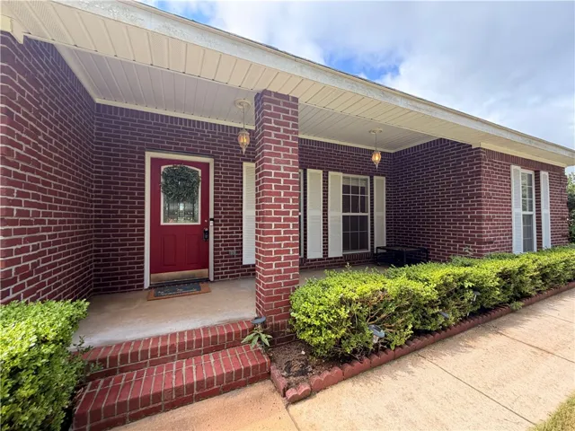 A welcoming brick facade with a vibrant red door offers timeless appeal and a shaded porch.