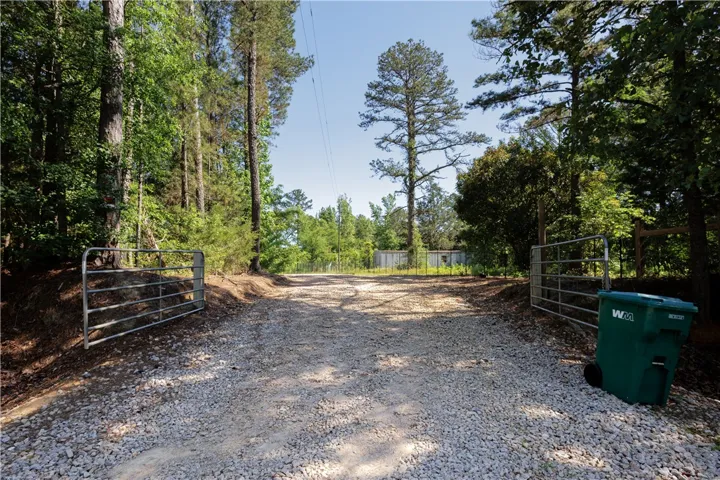 A private, gravel driveway opens into a verdant, wooded landscape.