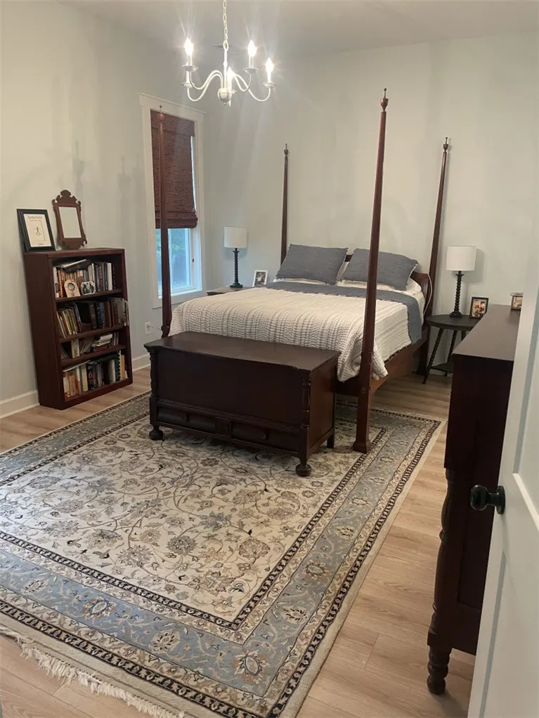 A well-lit bedroom features hardwood-style flooring and a charming chandelier.