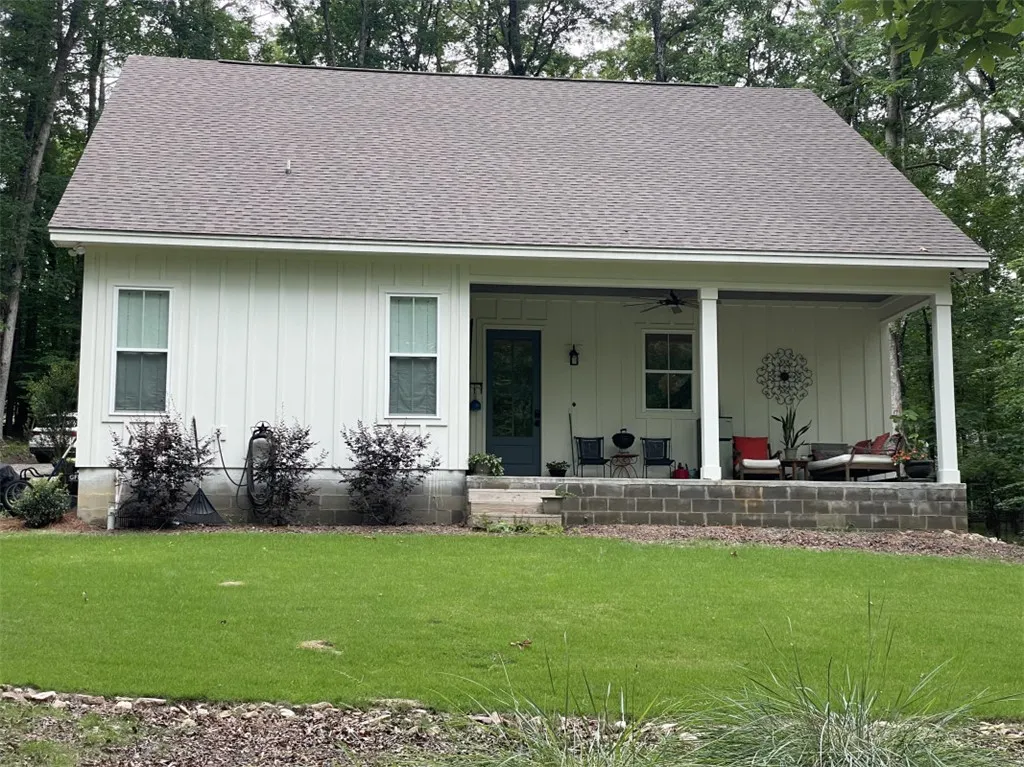 A welcoming front porch enhances this charming white board and batten home, nestled among mature trees.