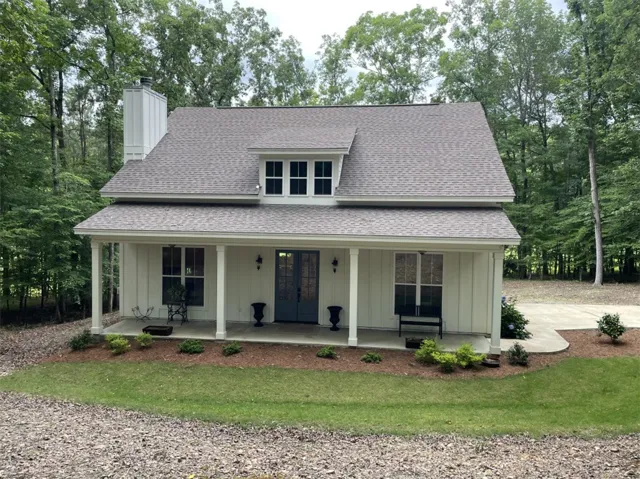 A charming facade welcomes with a covered porch and verdant surroundings, creating a peaceful retreat.